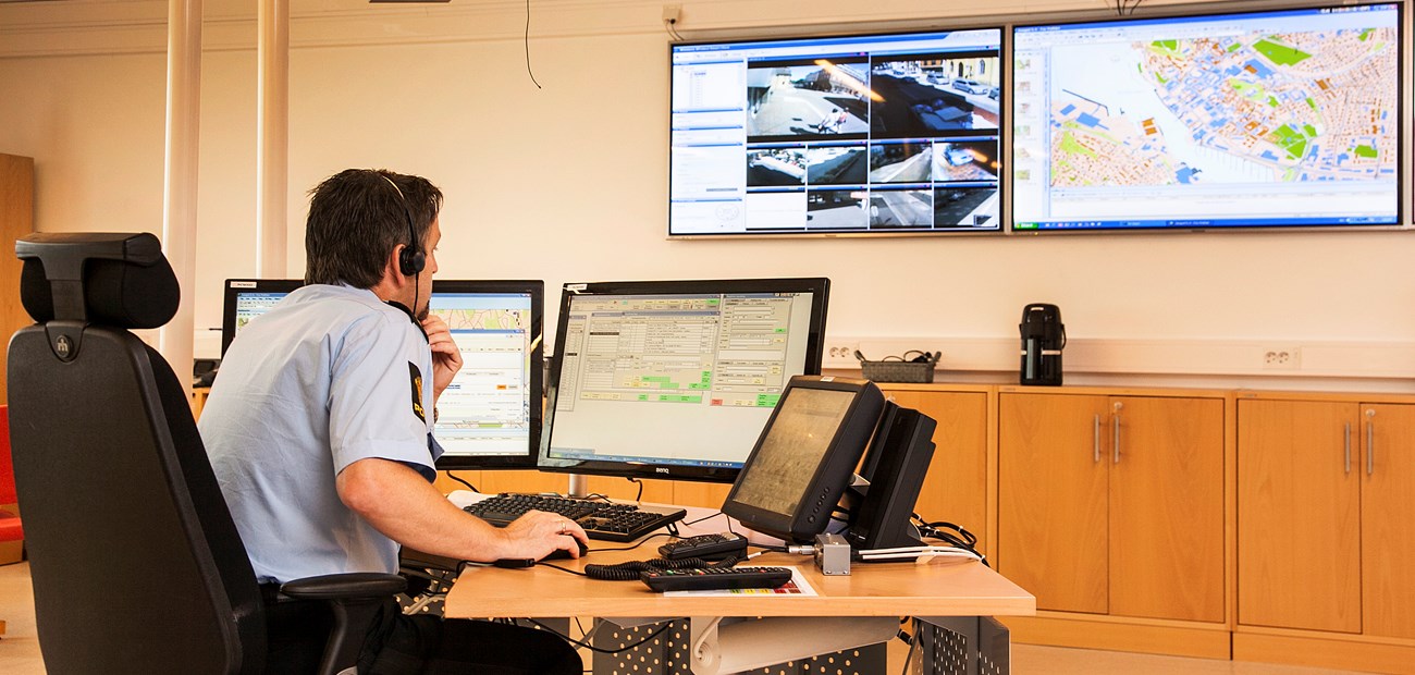 Bilde fra politiets operasjonssentral. En politimann sitter bak en rekke skjermer, og bruker ulike verktøy i oppdragshåndtering.
