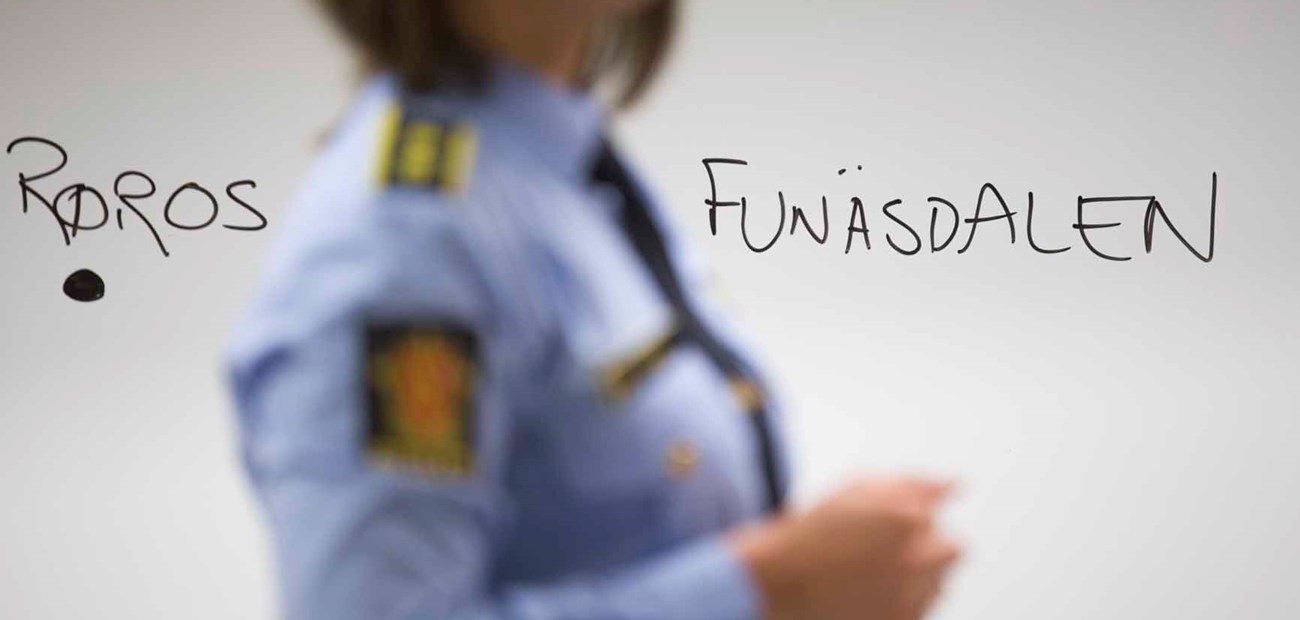 A policewoman stands in front of a whiteboard, on which Røros (Norway) and Funäsdalen (Sweden) are written.